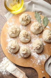 Photo of Uncooked khinkalis (dumplings) with flour, oil and bay leaves on wooden table, top view