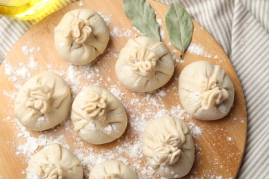 Photo of Uncooked khinkalis (dumplings) with flour and bay leaves on table, top view