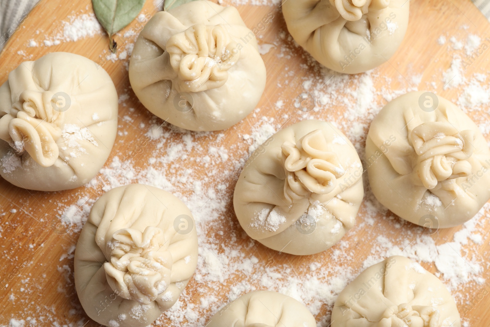Uncooked khinkalis (dumplings) with flour on wooden board, top view Photo of Uncooked khinkalis (dumplings) with flour on wooden board, top view