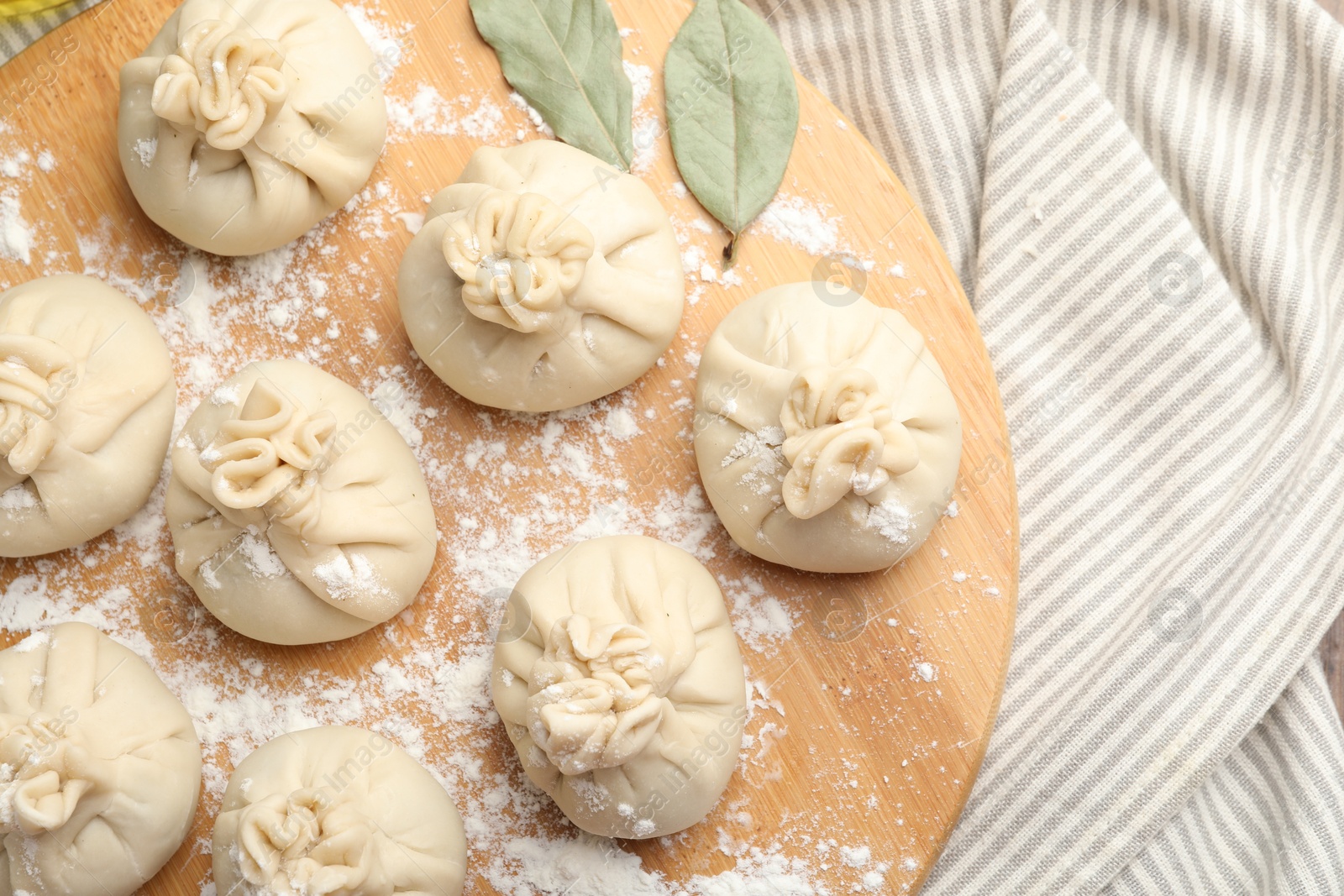 Uncooked khinkalis (dumplings) with flour and bay leaves on table, top view Photo of Uncooked khinkalis (dumplings) with flour and bay leaves on table, top view