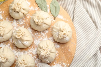 Photo of Uncooked khinkalis (dumplings) with flour and bay leaves on table, top view