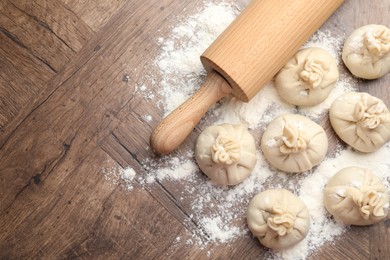 Photo of Uncooked khinkalis (dumplings) with rolling pin and flour on wooden table, flat lay. Space for text