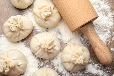 Photo of Uncooked khinkalis (dumplings) with rolling pin and flour on wooden table, flat lay
