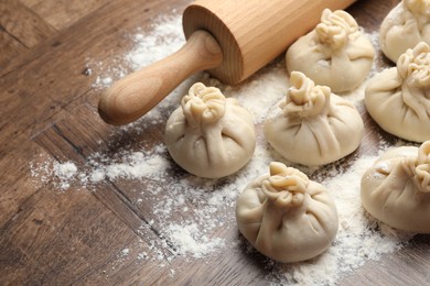 Photo of Uncooked khinkalis (dumplings) with rolling pin and flour on wooden table, closeup