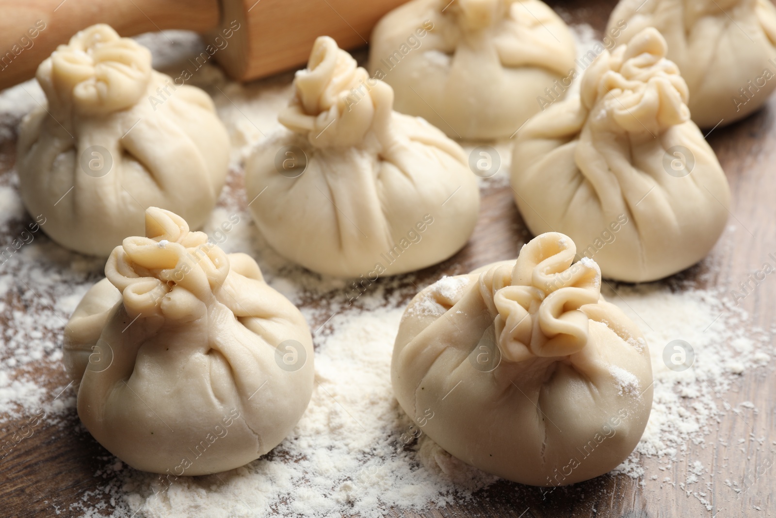 Uncooked khinkalis (dumplings) with flour on wooden table, closeup Photo of Uncooked khinkalis (dumplings) with flour on wooden table, closeup
