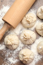 Photo of Uncooked khinkalis (dumplings) with rolling pin and flour on wooden table, flat lay