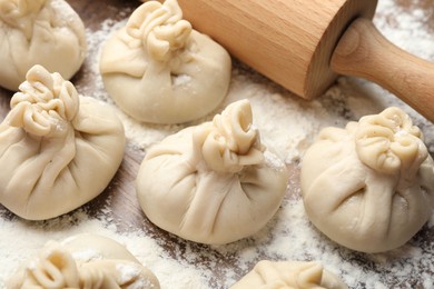 Photo of Uncooked khinkalis (dumplings) with rolling pin and flour on wooden table, closeup