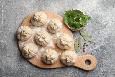 Photo of Uncooked khinkalis (dumplings) with peppercorns, flour, parsley and bay leaves on grey table, flat lay