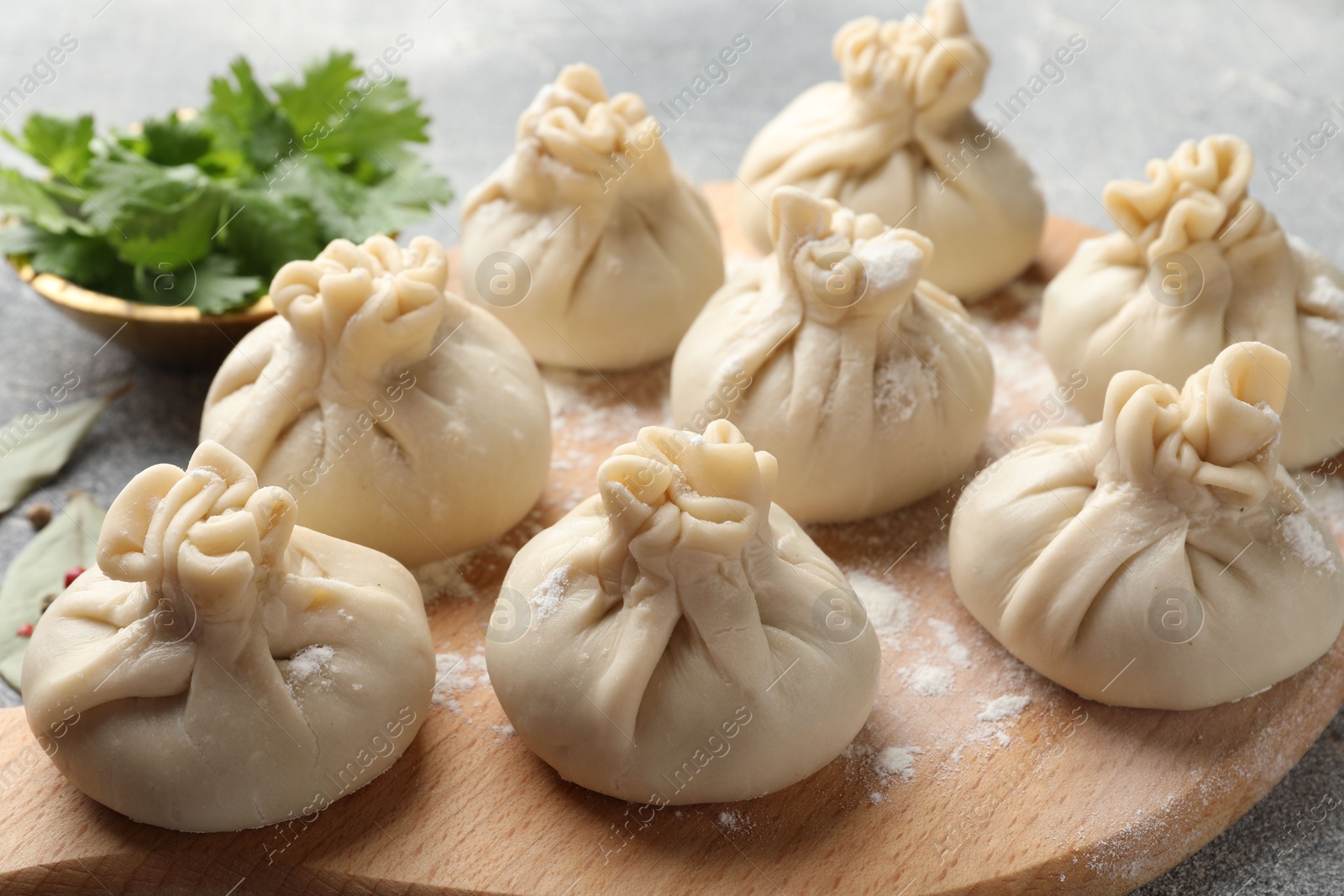 Uncooked khinkalis (dumplings) with flour and parsley on grey table, closeup Photo of Uncooked khinkalis (dumplings) with flour and parsley on grey table, closeup