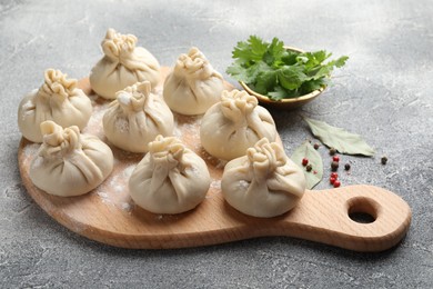 Photo of Uncooked khinkalis (dumplings) with peppercorns, flour, parsley and bay leaves on grey table