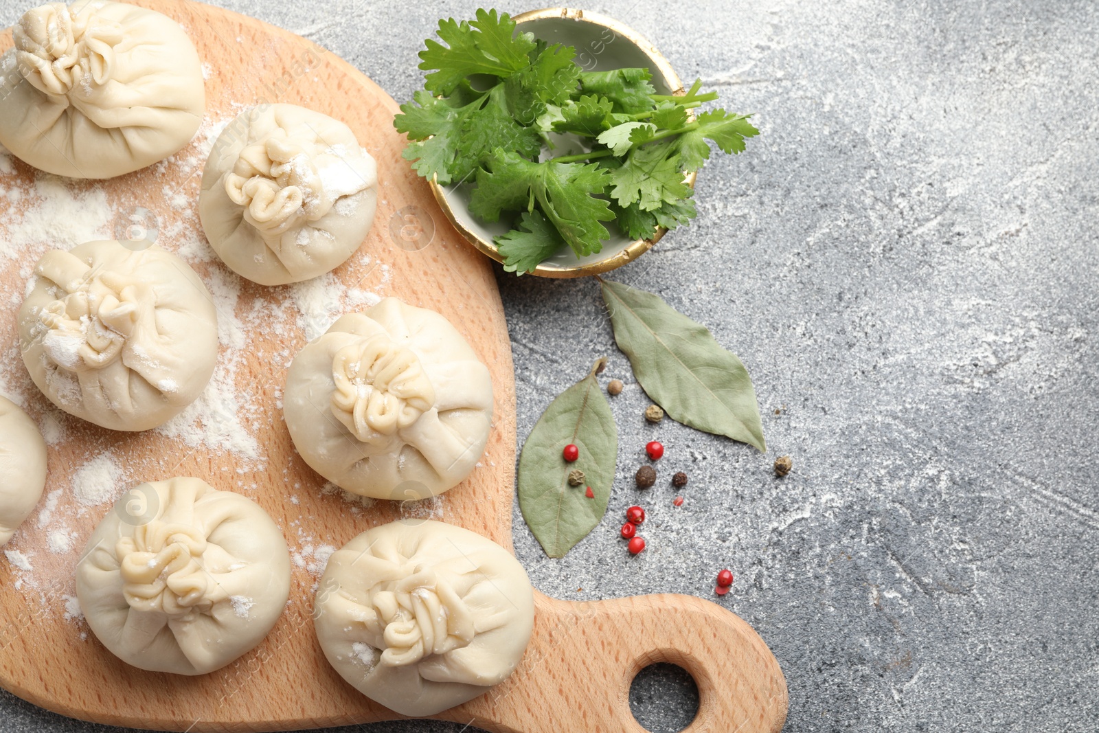 Uncooked khinkalis (dumplings) with peppercorns, flour, parsley and bay leaves on grey table, flat lay. Space for text Photo of Uncooked khinkalis (dumplings) with peppercorns, flour, parsley and bay leaves on grey table, flat lay. Space for text