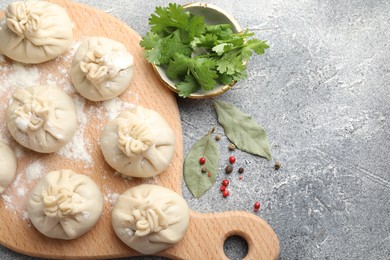 Photo of Uncooked khinkalis (dumplings) with peppercorns, flour, parsley and bay leaves on grey table, flat lay. Space for text