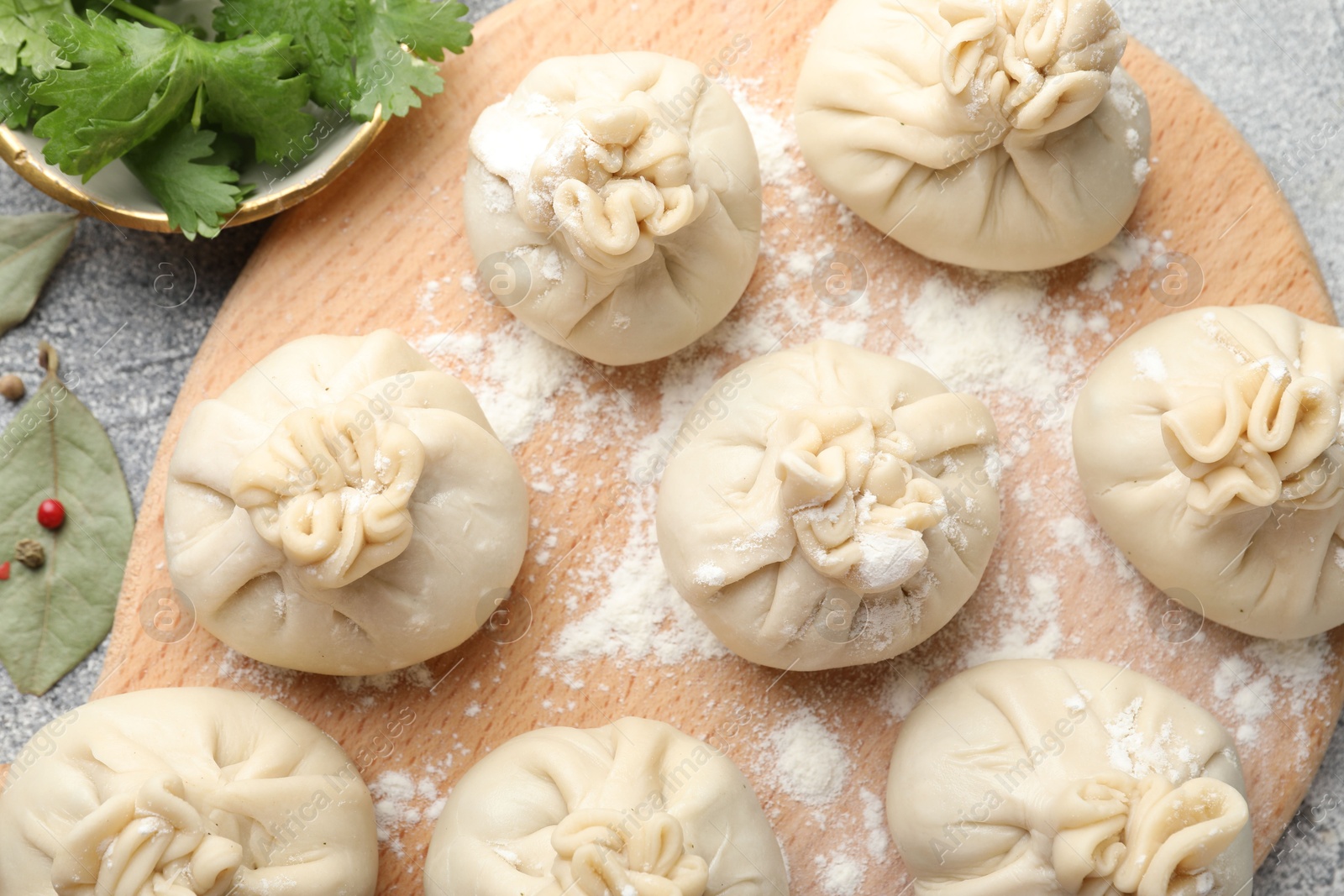 Uncooked khinkalis (dumplings) with peppercorns, flour, parsley and bay leaves on grey table, flat lay Photo of Uncooked khinkalis (dumplings) with peppercorns, flour, parsley and bay leaves on grey table, flat lay