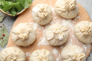 Photo of Uncooked khinkalis (dumplings) with peppercorns, flour, parsley and bay leaves on grey table, flat lay