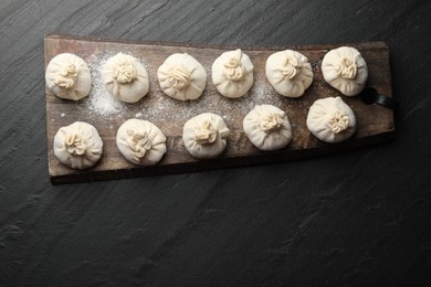 Photo of Uncooked khinkalis (dumplings) with flour on black table, top view. Space for text