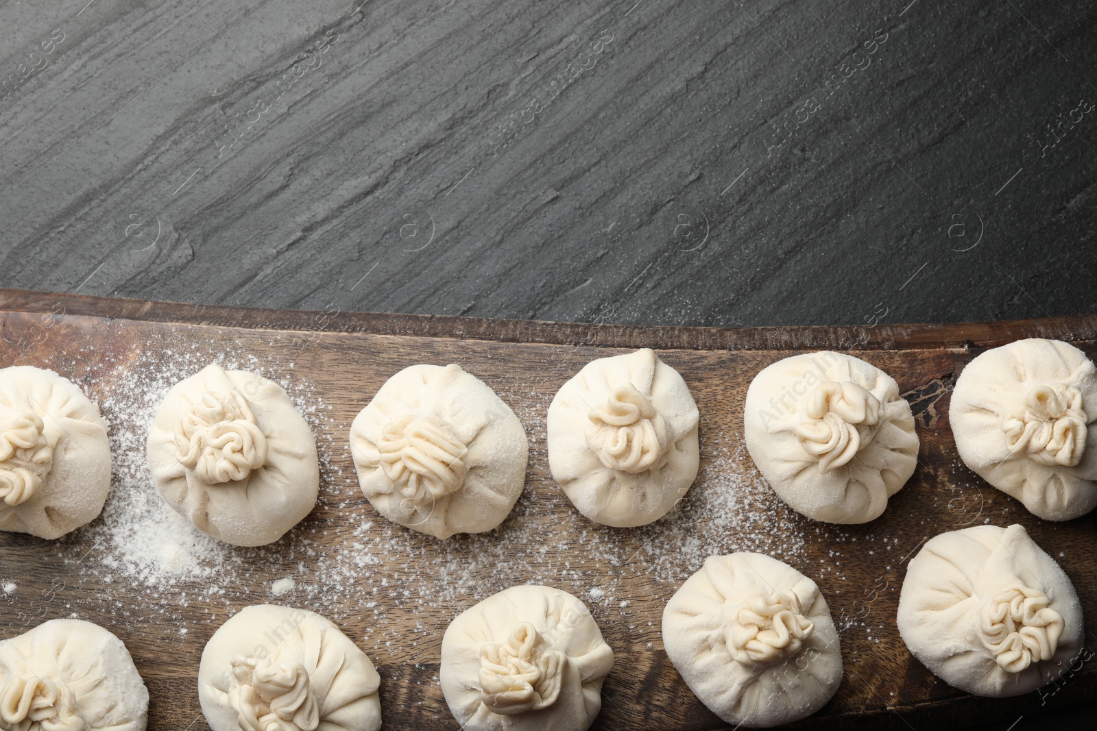 Uncooked khinkalis (dumplings) with flour on black table, top view. Space for text Photo of Uncooked khinkalis (dumplings) with flour on black table, top view. Space for text