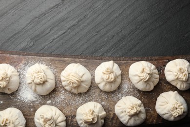 Photo of Uncooked khinkalis (dumplings) with flour on black table, top view. Space for text