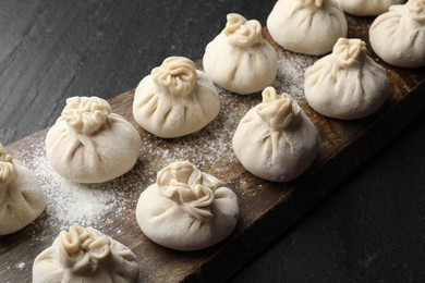 Photo of Uncooked khinkalis (dumplings) with flour on black table, closeup