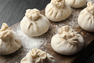 Photo of Uncooked khinkalis (dumplings) with flour on black table, closeup