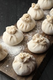 Photo of Uncooked khinkalis (dumplings) with flour on black table, closeup