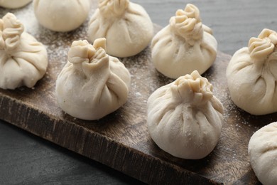 Photo of Uncooked khinkalis (dumplings) with flour on black table, closeup