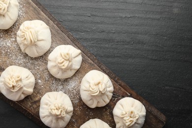 Photo of Uncooked khinkalis (dumplings) with flour on black table, top view. Space for text