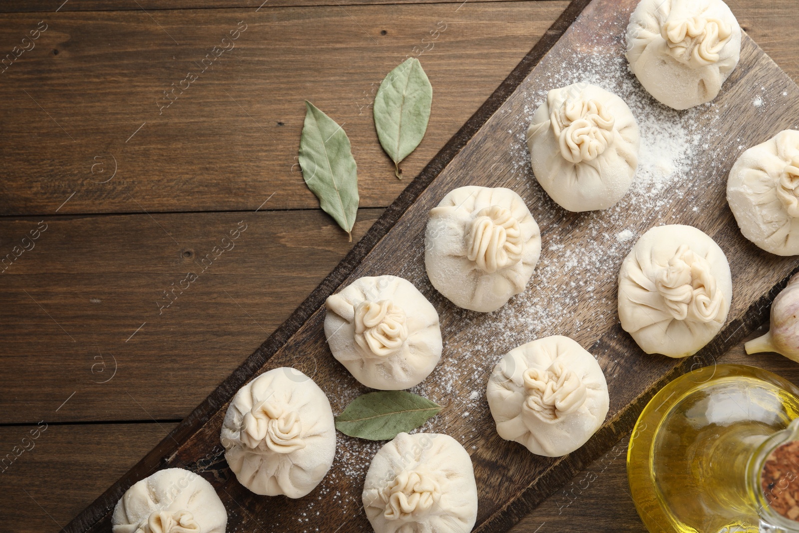 Uncooked khinkalis (dumplings) with flour, garlic and bay leaves on wooden table, flat lay Photo of Uncooked khinkalis (dumplings) with flour, garlic and bay leaves on wooden table, flat lay
