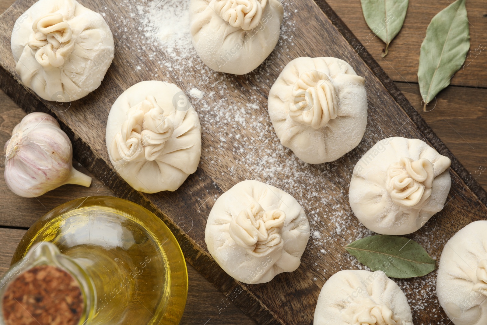 Uncooked khinkalis (dumplings) with flour, oil and bay leaves on wooden table, flat lay Photo of Uncooked khinkalis (dumplings) with flour, oil and bay leaves on wooden table, flat lay
