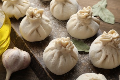 Photo of Uncooked khinkalis (dumplings) with flour, garlic and bay leaves on wooden table, closeup