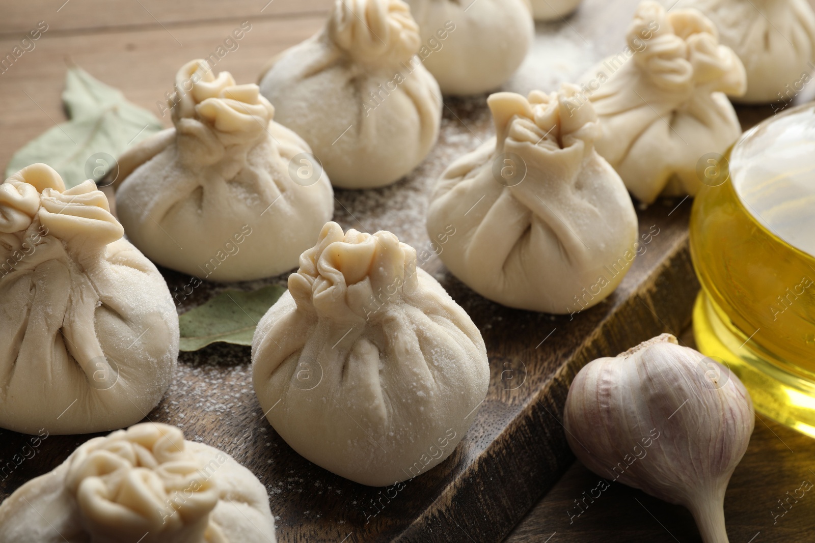 Uncooked khinkalis (dumplings) with flour, garlic and bay leaves on wooden table, closeup Photo of Uncooked khinkalis (dumplings) with flour, garlic and bay leaves on wooden table, closeup