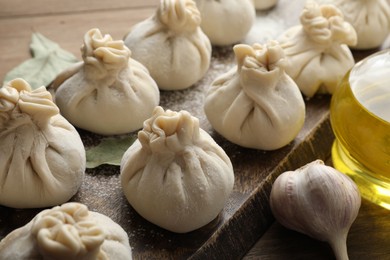 Photo of Uncooked khinkalis (dumplings) with flour, garlic and bay leaves on wooden table, closeup