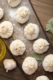 Photo of Uncooked khinkalis (dumplings) with flour, garlic and bay leaves on wooden table, flat lay