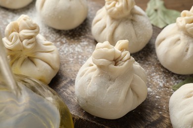 Photo of Uncooked khinkalis (dumplings) with flour and bay leaves on wooden table, closeup