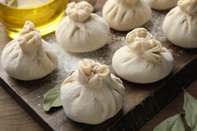 Photo of Uncooked khinkalis (dumplings) with flour and bay leaves on wooden table, closeup