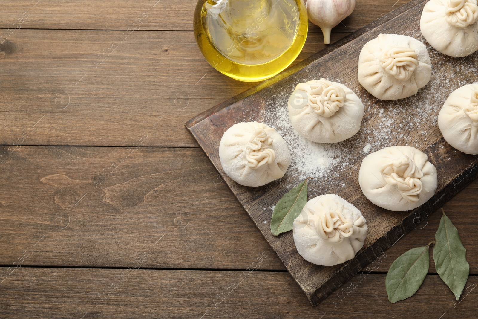 Uncooked khinkalis (dumplings) with flour, garlic and bay leaves on wooden table, flat lay. Space for text Photo of Uncooked khinkalis (dumplings) with flour, garlic and bay leaves on wooden table, flat lay. Space for text