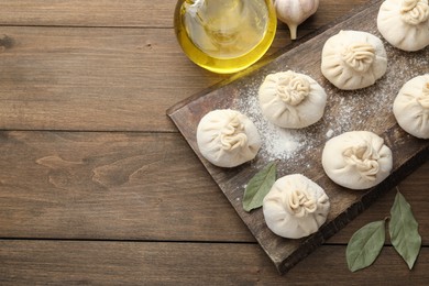 Photo of Uncooked khinkalis (dumplings) with flour, garlic and bay leaves on wooden table, flat lay. Space for text