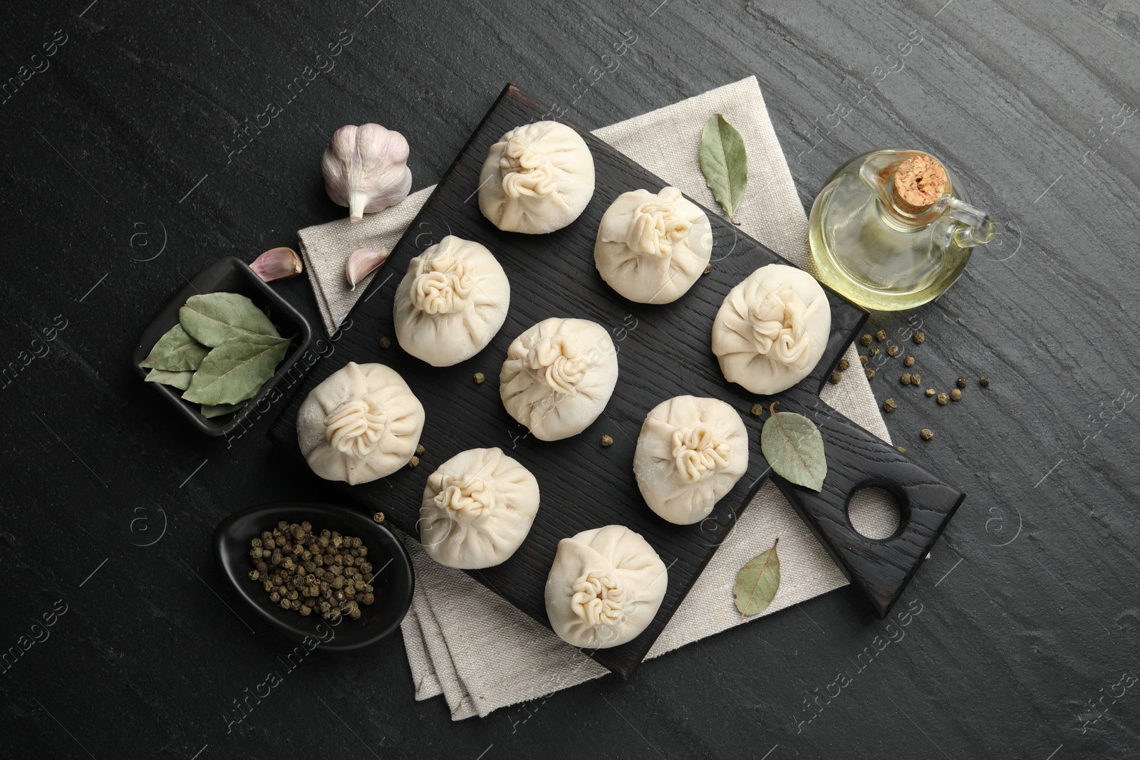 Uncooked khinkalis (dumplings) with peppercorns, garlic and bay leaves on black table, flat lay Photo of Uncooked khinkalis (dumplings) with peppercorns, garlic and bay leaves on black table, flat lay