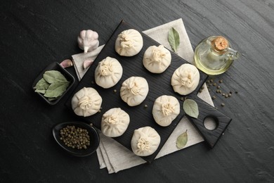 Photo of Uncooked khinkalis (dumplings) with peppercorns, garlic and bay leaves on black table, flat lay