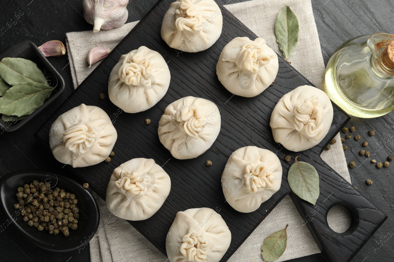 Uncooked khinkalis (dumplings) with peppercorns, garlic and bay leaves on black table, flat lay Photo of Uncooked khinkalis (dumplings) with peppercorns, garlic and bay leaves on black table, flat lay
