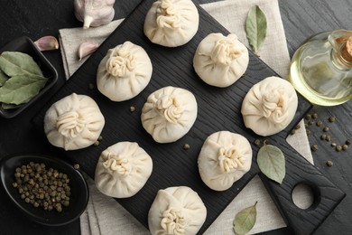 Photo of Uncooked khinkalis (dumplings) with peppercorns, garlic and bay leaves on black table, flat lay
