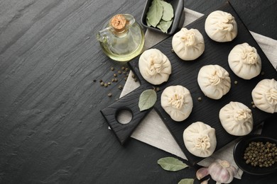 Photo of Uncooked khinkalis (dumplings) with peppercorns, garlic and bay leaves on black table, flat lay. Space for text