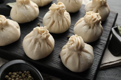Photo of Uncooked khinkalis (dumplings) with peppercorns on black table, closeup