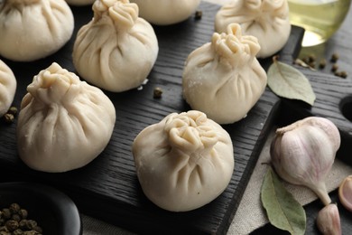 Photo of Uncooked khinkalis (dumplings) with peppercorns, garlic and bay leaves on black table, closeup