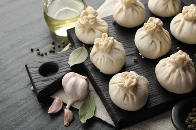 Photo of Uncooked khinkalis (dumplings) with peppercorns, garlic and bay leaves on black table, closeup