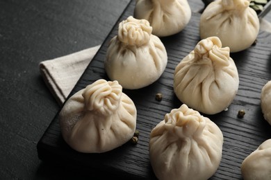 Photo of Uncooked khinkalis (dumplings) with peppercorns on black table, closeup
