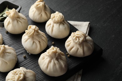 Photo of Uncooked khinkalis (dumplings) with peppercorns on black table, closeup