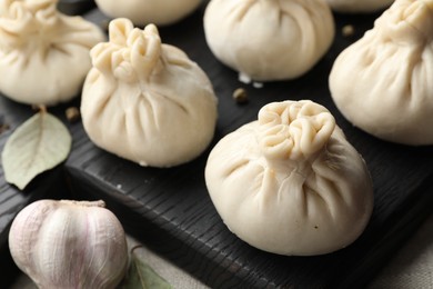Photo of Uncooked khinkalis (dumplings) with peppercorns, garlic and bay leaves on table, closeup