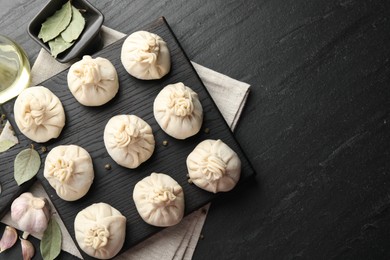 Photo of Uncooked khinkalis (dumplings) with peppercorns, garlic and bay leaves on black table, flat lay. Space for text