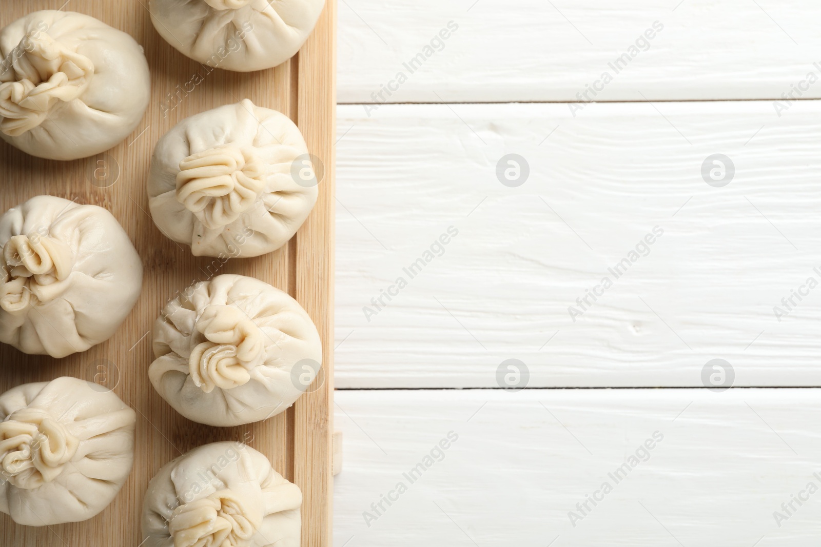 Photo of Uncooked khinkalis (dumplings) on white wooden table, top view. Space for text