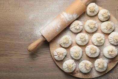 Photo of Uncooked khinkalis (dumplings) and rolling pin on wooden table, top view. Space for text